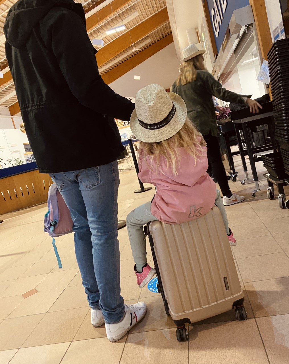 Liten flicka med stråhatt sitter på en kabinväska i väntan på att få flyga på semester.