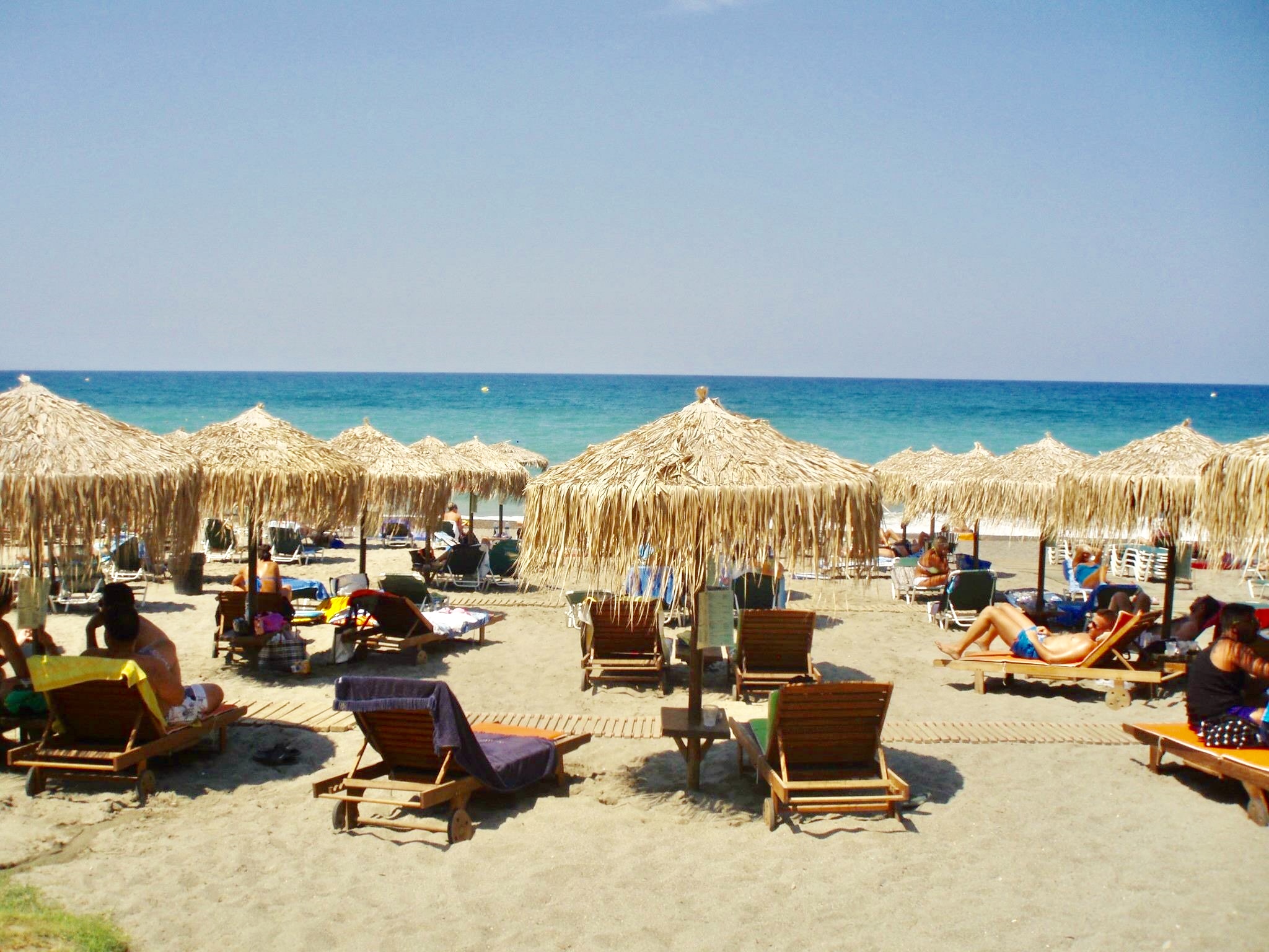 Sandstrand med solstolar och parasoll på Kreta
