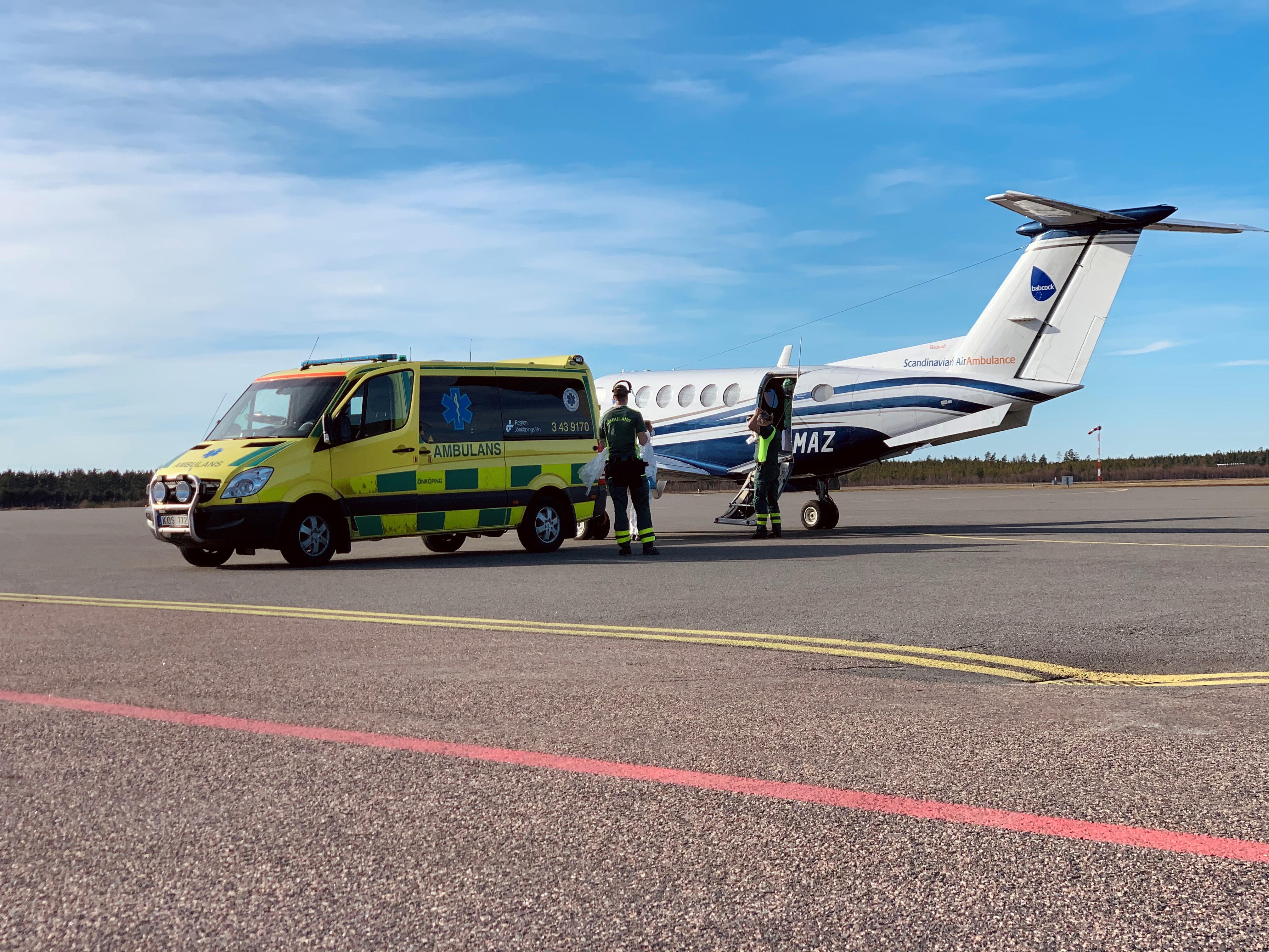 Sjukvårdspersonal  invid en ambulans och ett ambulansflygplan parkerat på flygplansplattan